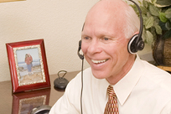 Dr. Merlin Switzer using headphones in front of the computer providing coaching over the phone with the banner, Coaching for Leadership Success, written on the screen.